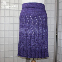Load image into Gallery viewer, An image of a knitted skirt with lacy zig zags running down the pleats. Knitted in Ancient Arts Merino + Silk.