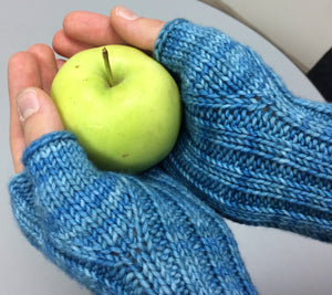 Hands wearing Eve's wristwarmers in RCY Eden colour River and holding an apple